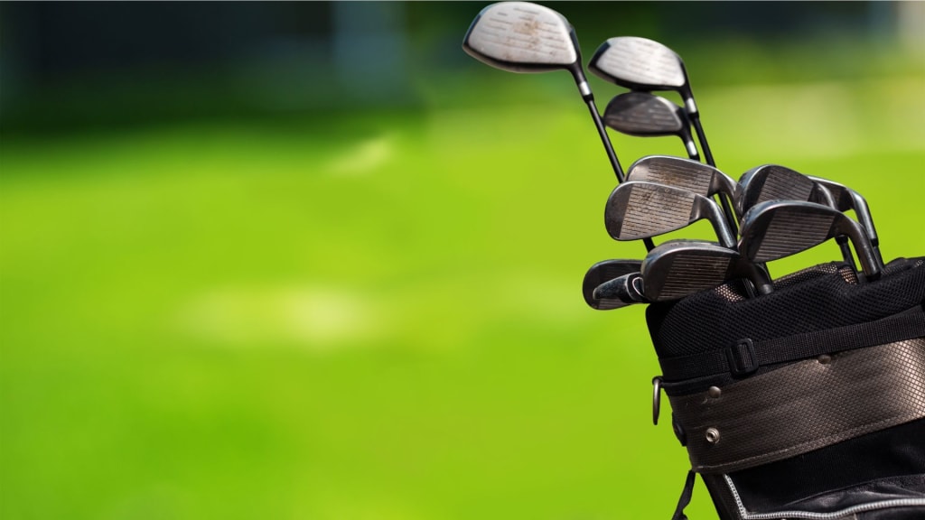 Close-up of a set of golf clubs in a bag with a blurred green background.